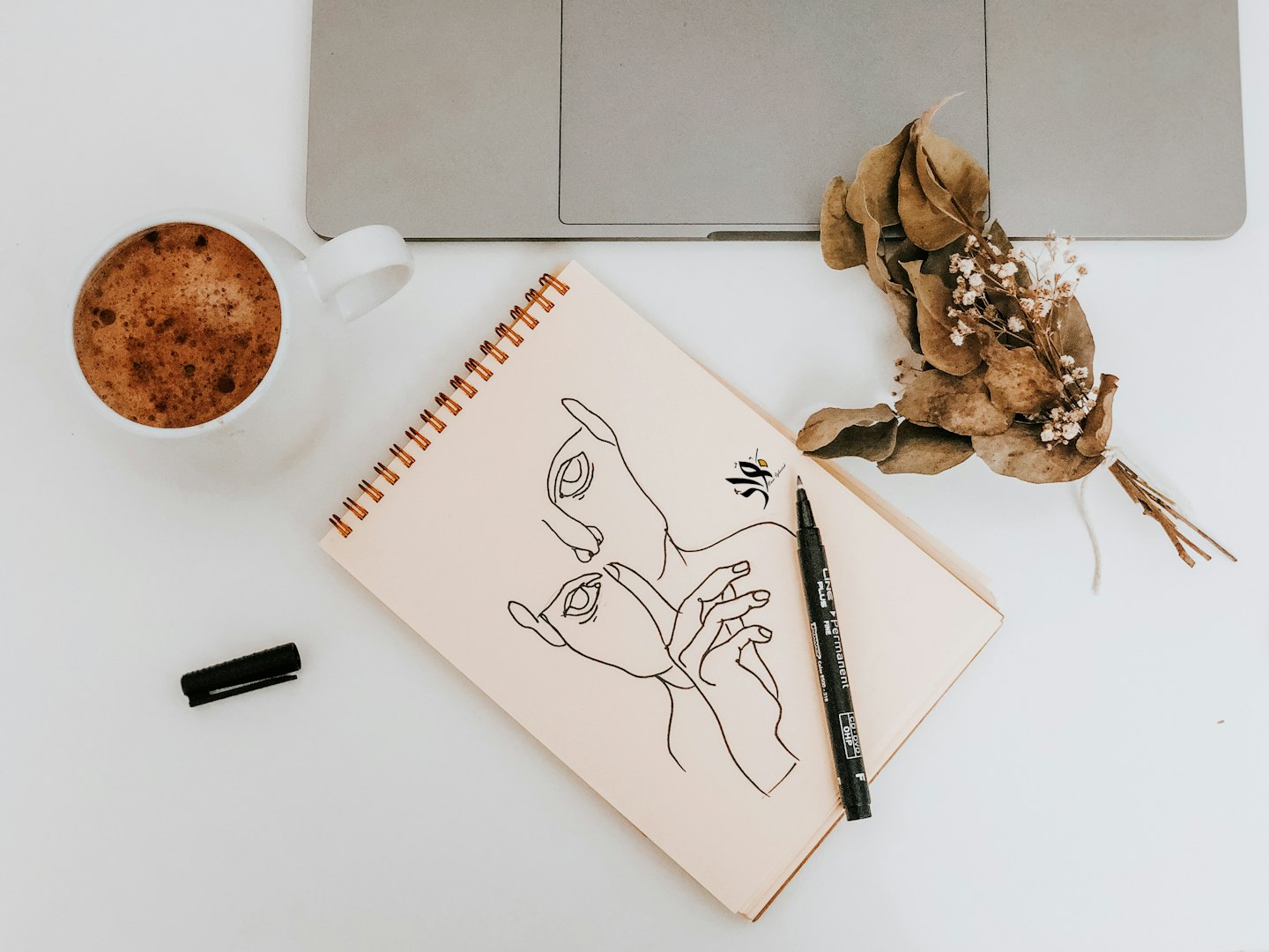 Caffè, computer portatile e taccuino con schizzi su una scrivania.