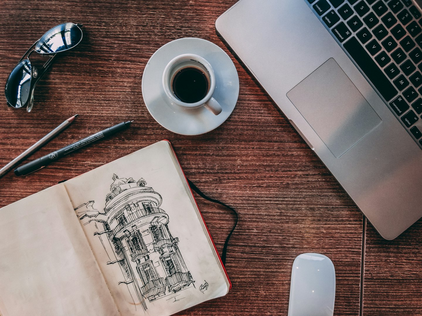 Spazio di lavoro creativo con taccuino, laptop e caffè su tavolo di legno.