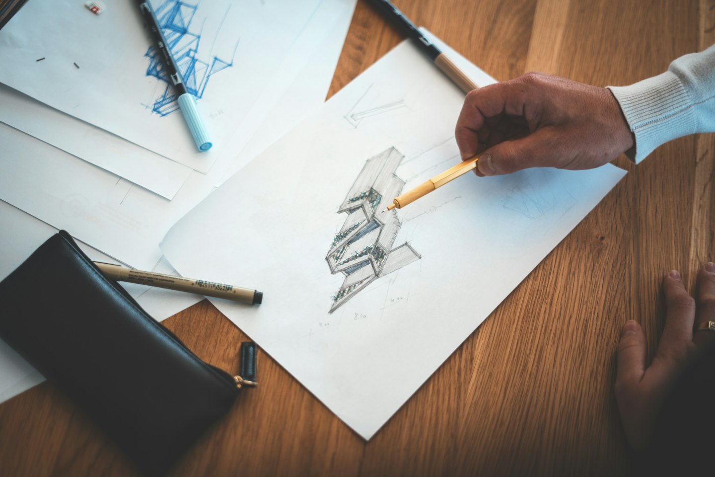 Mani che disegnano progetti architettonici su carta bianca con una penna arancione.
